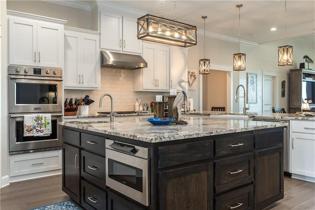 kitchen with under cabinet range hood, a kitchen island with sink, white cabinetry, and stainless steel double oven