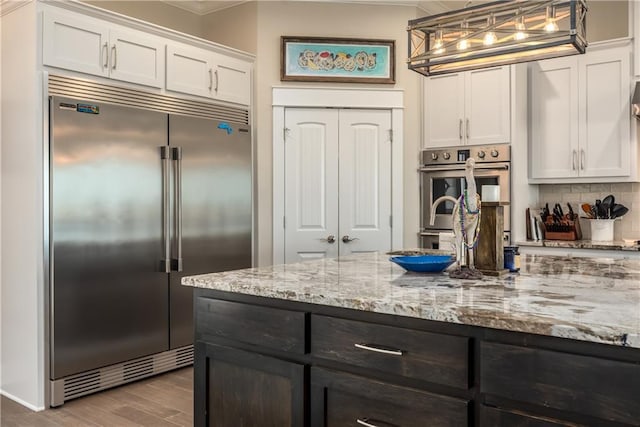 kitchen featuring light stone counters, wood finished floors, stainless steel appliances, white cabinetry, and backsplash