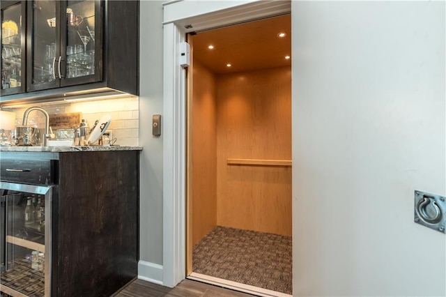 bar with tasteful backsplash, elevator, wine cooler, indoor wet bar, and a sink