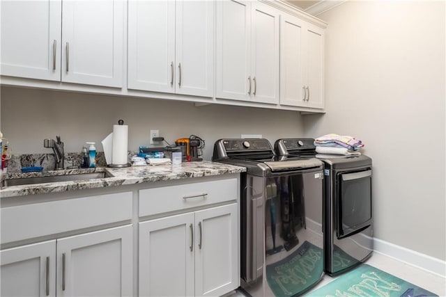 clothes washing area featuring cabinet space, a sink, washer and clothes dryer, and baseboards