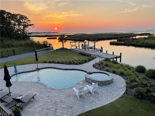 pool at dusk featuring a patio, a water view, a dock, fence, and a pool with connected hot tub