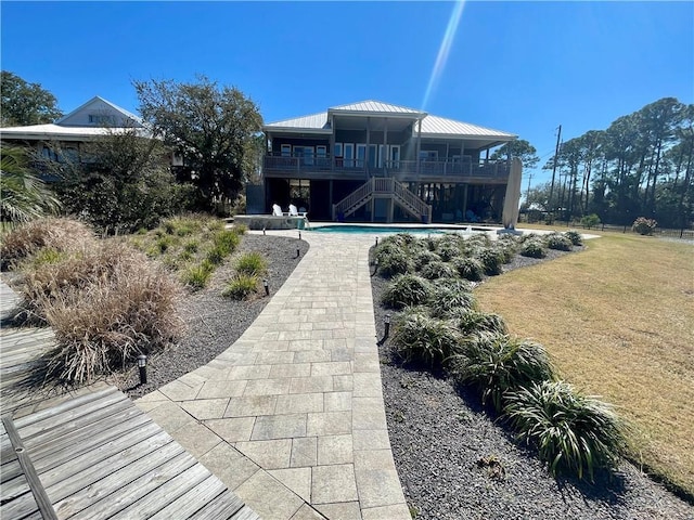 rear view of house with stairs, metal roof, a yard, and an outdoor pool