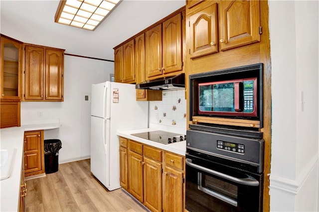 kitchen with light wood-type flooring, black appliances, and backsplash