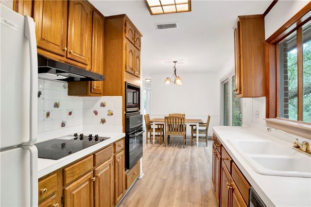 kitchen featuring tasteful backsplash, black appliances, sink, hanging light fixtures, and light hardwood / wood-style floors