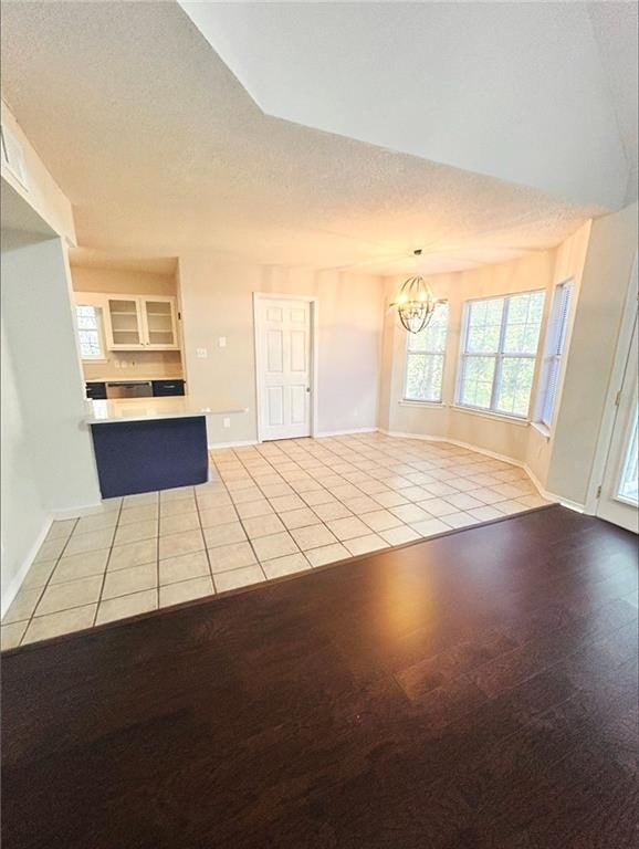 unfurnished living room featuring a notable chandelier, a textured ceiling, and light tile patterned floors