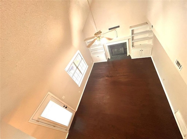 unfurnished living room with built in features, a high ceiling, and ceiling fan