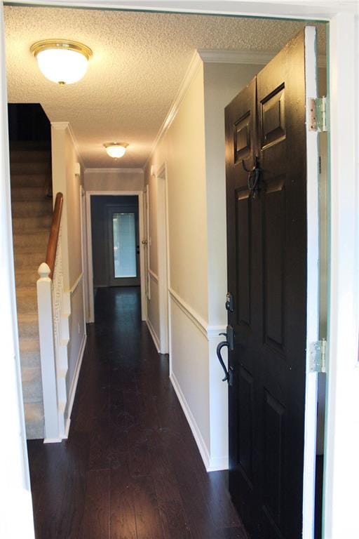 corridor with dark wood-type flooring, ornamental molding, and a textured ceiling