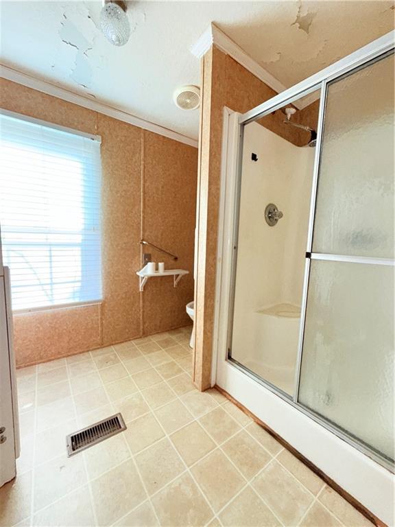 bathroom with ornamental molding, visible vents, a shower with door, and toilet