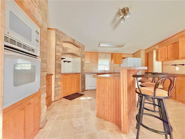 kitchen with a textured ceiling, white appliances, a sink, light countertops, and a kitchen bar