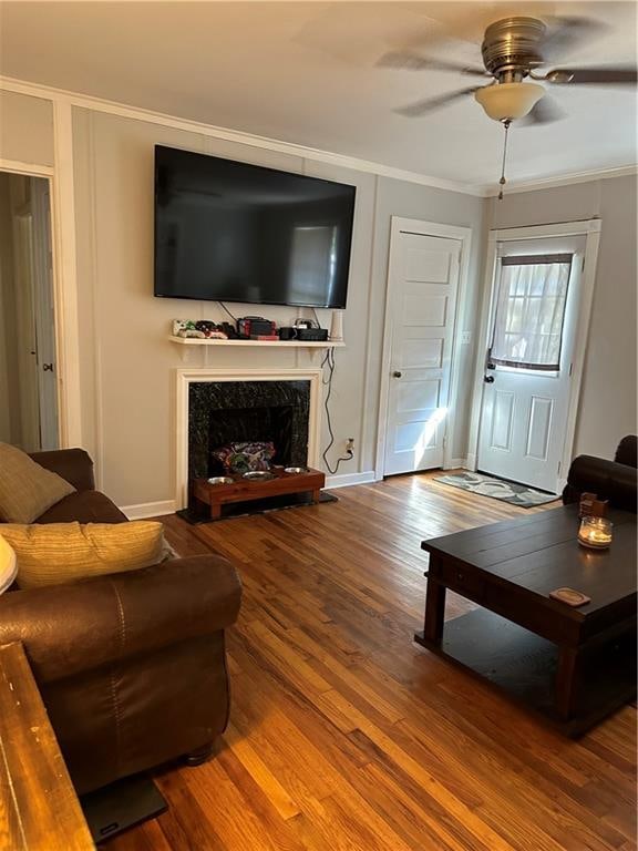 living room with ceiling fan, hardwood / wood-style floors, a premium fireplace, and ornamental molding