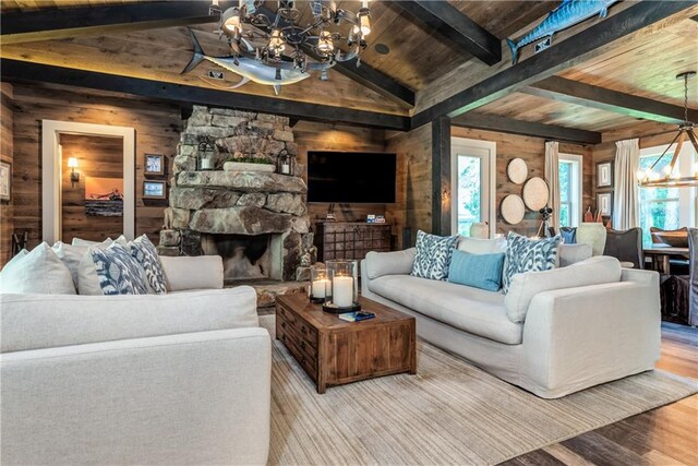 living room with wood-type flooring, a stone fireplace, wooden walls, and a chandelier