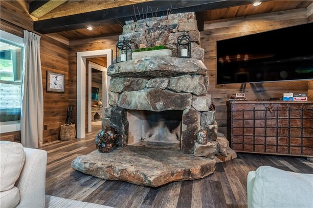 living room featuring hardwood / wood-style flooring, wood ceiling, beamed ceiling, a stone fireplace, and wood walls