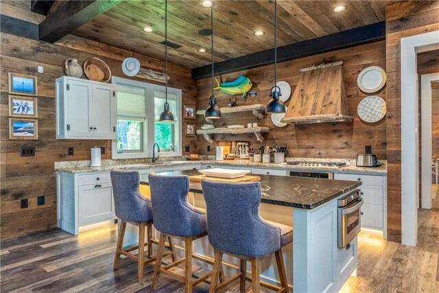 kitchen featuring wood walls, pendant lighting, hardwood / wood-style flooring, and white cabinetry