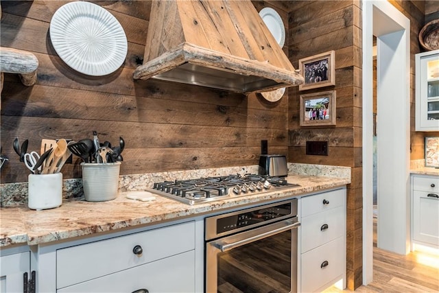 kitchen featuring custom range hood, appliances with stainless steel finishes, white cabinets, and light hardwood / wood-style floors