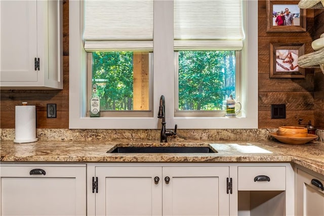 kitchen with white cabinets, a wealth of natural light, light stone counters, and sink