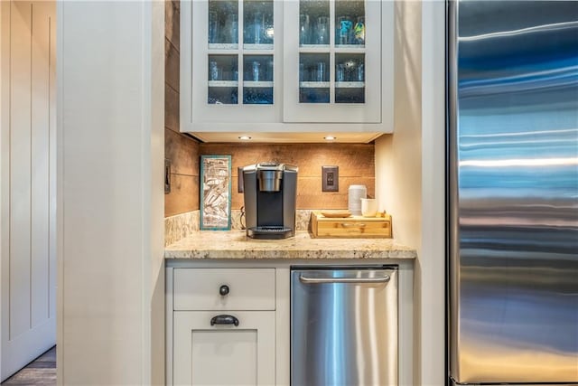 bar with stainless steel built in refrigerator, hardwood / wood-style floors, decorative backsplash, white cabinetry, and light stone counters