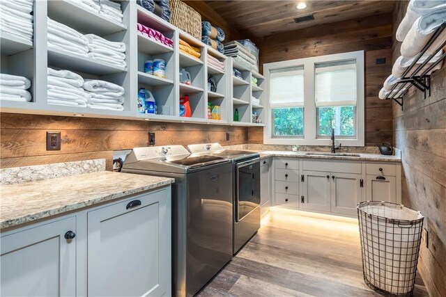 clothes washing area with wooden ceiling, light hardwood / wood-style flooring, sink, washing machine and dryer, and wooden walls