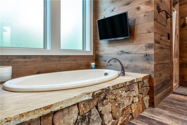 bathroom featuring wood-type flooring, wooden walls, and a washtub