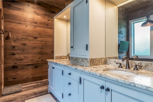 full bath with double vanity, wood finished floors, wood walls, and a sink