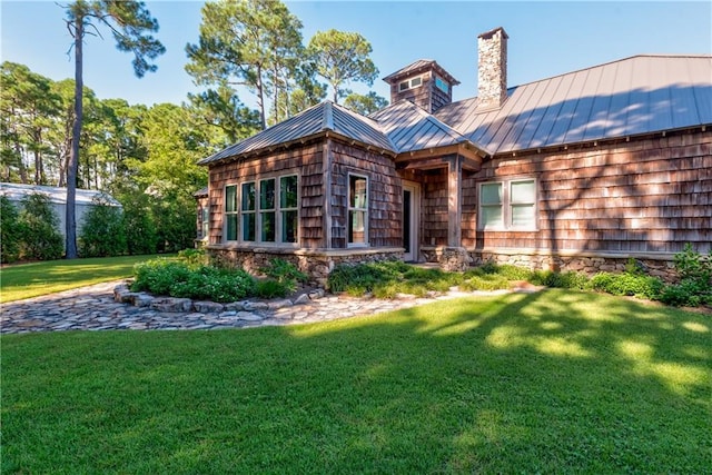 back of property featuring a standing seam roof, a lawn, a chimney, and metal roof