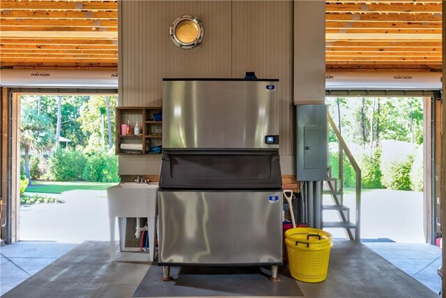 kitchen with stainless steel refrigerator, concrete flooring, and electric panel