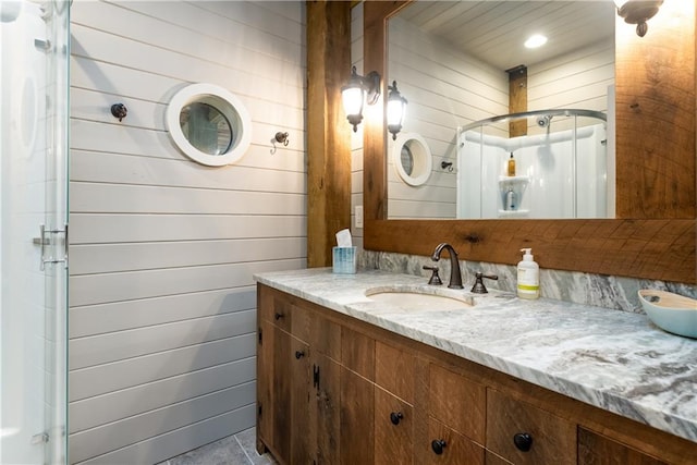 bathroom featuring vanity, a shower with shower door, and wooden walls