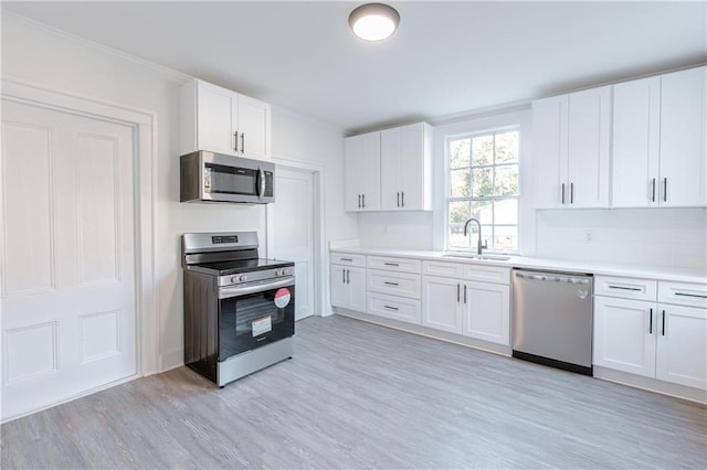 kitchen with tasteful backsplash, sink, white cabinets, stainless steel appliances, and light wood-type flooring