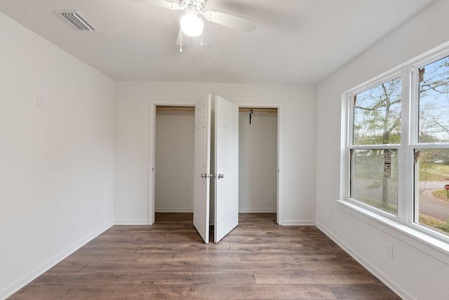 unfurnished bedroom featuring ceiling fan, dark hardwood / wood-style flooring, and two closets