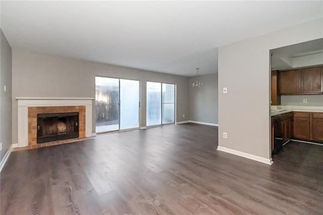 unfurnished living room featuring dark wood-style floors, a fireplace, an inviting chandelier, and baseboards