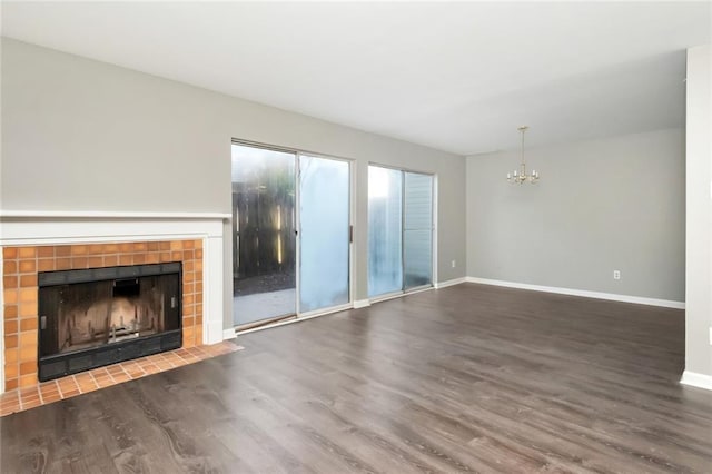 unfurnished living room featuring a notable chandelier, a tiled fireplace, wood finished floors, and baseboards