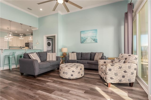 living room featuring stacked washing maching and dryer, visible vents, crown molding, and wood finished floors