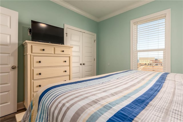 bedroom with a closet, crown molding, baseboards, and wood finished floors