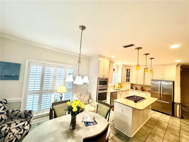 kitchen featuring a kitchen breakfast bar, ornamental molding, stainless steel appliances, sink, and decorative light fixtures