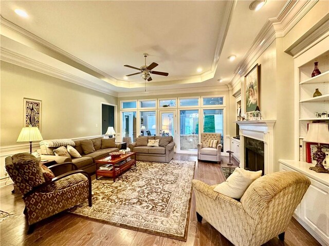 living room with a high end fireplace, a tray ceiling, ceiling fan, dark wood-type flooring, and built in features