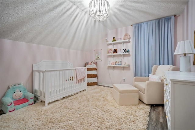bedroom featuring a notable chandelier, vaulted ceiling, a textured ceiling, a crib, and wood finished floors