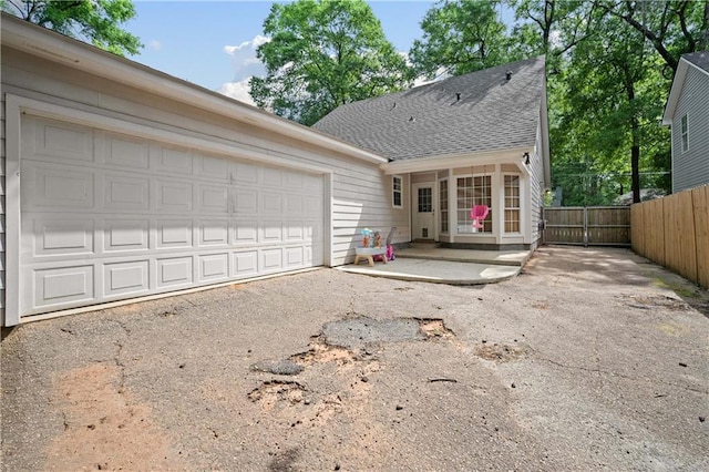 exterior space with fence, driveway, an attached garage, and roof with shingles