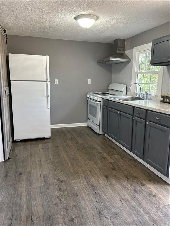 kitchen with wall chimney range hood, white appliances, sink, gray cabinetry, and dark hardwood / wood-style floors