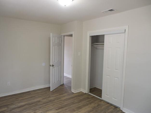 unfurnished bedroom featuring a closet, visible vents, baseboards, and dark wood-type flooring