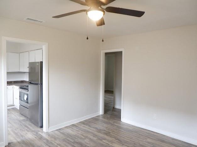 spare room featuring baseboards, a ceiling fan, visible vents, and light wood-style floors