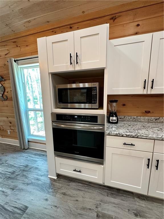 1401 Osprey Ln, Dauphin Island, AL 36528 - kitchen featuring wood finished floors, wooden walls, white cabinets, light stone counters, and stainless steel appliances