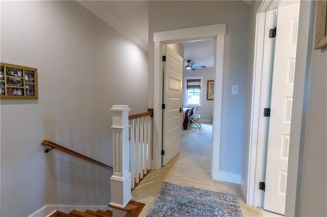 hall with an upstairs landing, baseboards, and light carpet