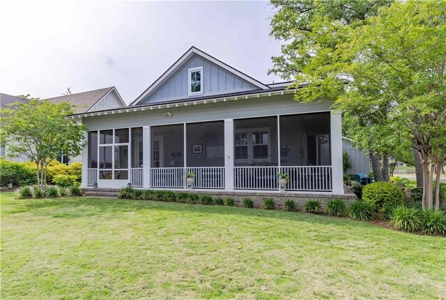 back of property with board and batten siding, a sunroom, and a lawn