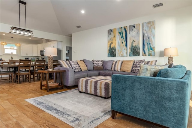 living room featuring light wood finished floors, visible vents, and vaulted ceiling
