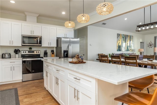 kitchen featuring pendant lighting, appliances with stainless steel finishes, a kitchen island, and white cabinets