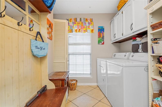 clothes washing area with cabinets, light tile patterned floors, wood walls, and washing machine and clothes dryer