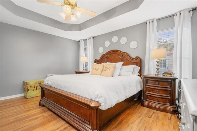 bedroom with light hardwood / wood-style floors, a raised ceiling, and ceiling fan