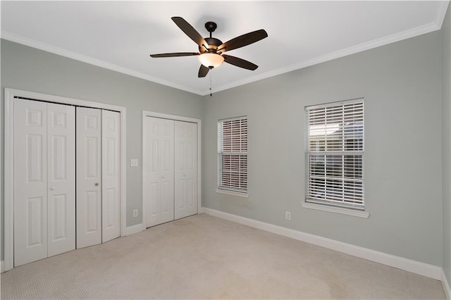 unfurnished bedroom with ceiling fan, multiple closets, ornamental molding, and light carpet