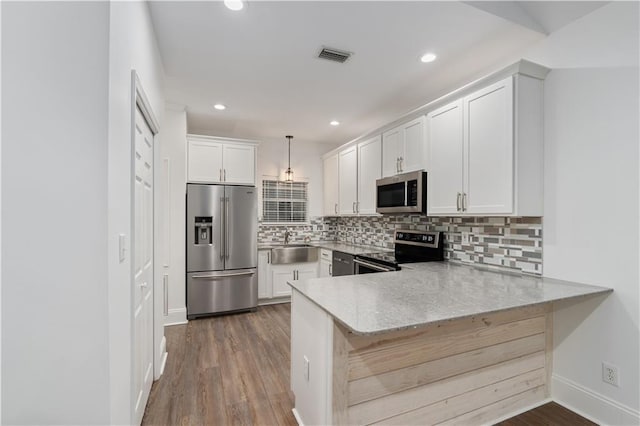 kitchen with appliances with stainless steel finishes, white cabinets, kitchen peninsula, and hardwood / wood-style flooring