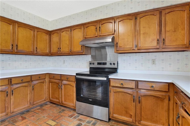 10437 Traci Dr, Semmes, AL 36575 - kitchen featuring brown cabinetry, stainless steel electric range oven, brick floor, under cabinet range hood, and wallpapered walls