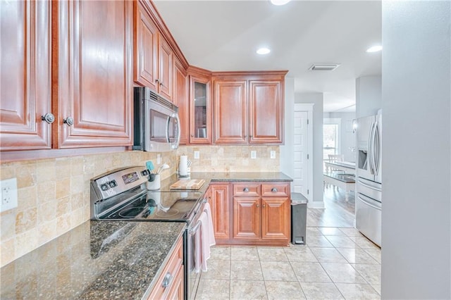 kitchen featuring decorative backsplash, stainless steel appliances, dark stone counters, and light tile patterned flooring